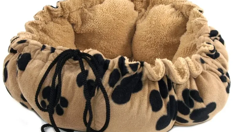 Manta redonda de felpa beige con huellas negras impresas y un cordón que la recoge y la convierte en cesto