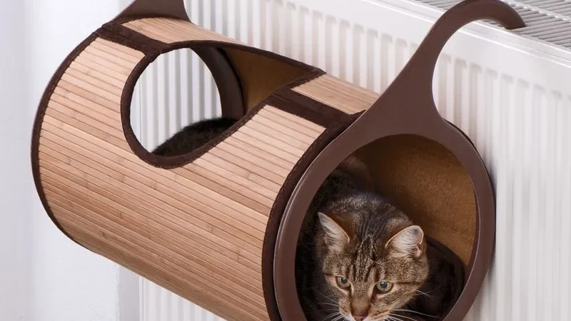 Hamaca Natural Retreat de láminas de bambú colgada de un radiador con sus ganchos laterales, con un gato atigrado tumbado dentro